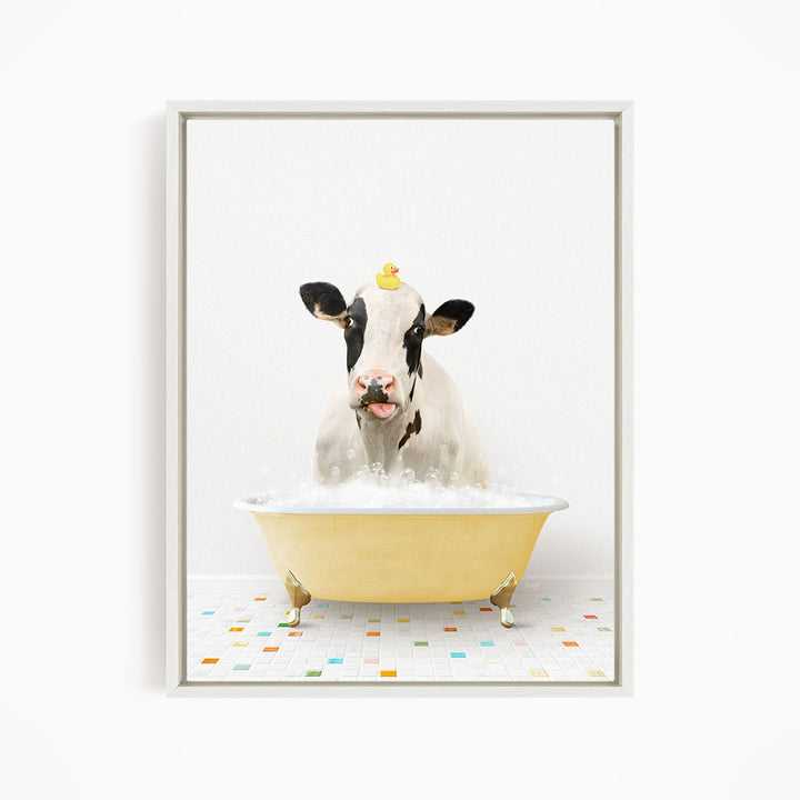 A black and white cow is sitting in a yellow bathtub filled with bubbles, with a yellow rubber duck perched on its head.