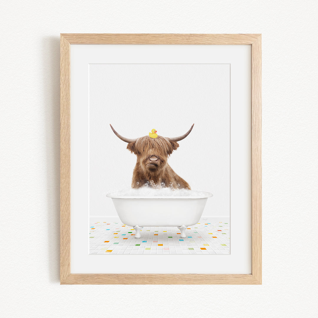 A brown cow with long horns is sitting in a white bathtub filled with bubbles, with a yellow rubber duck perched on its head.
