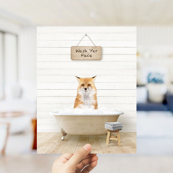 A hand holds up a framed image of a cat sitting in a bathtub, with a sign above that says "Wash Your Face".