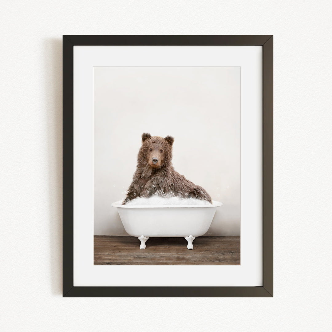A brown bear sitting in a white bathtub filled with water, looking directly at the camera.