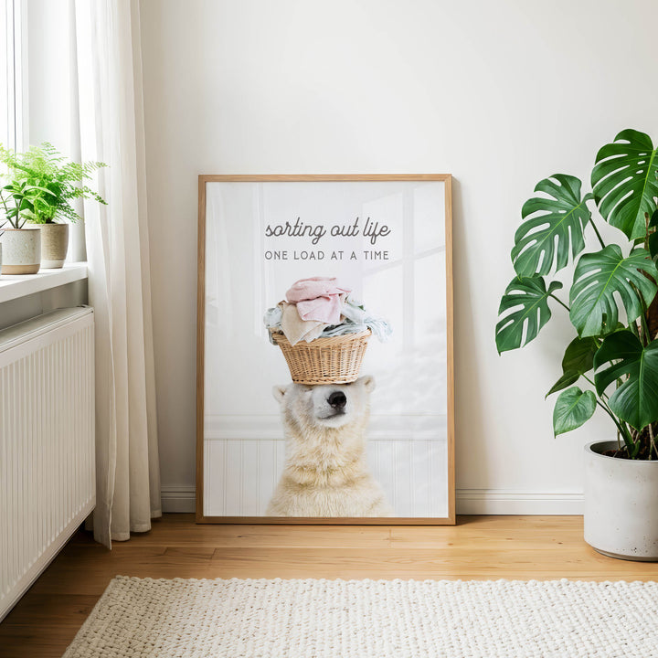 A framed poster with a polar bear holding a basket of laundry, accompanied by the text "sorting out life one load at a time".