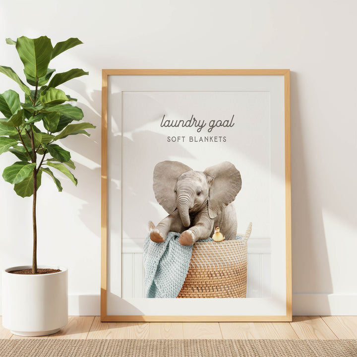 A framed image of an elephant sitting in a basket, with the text "laundry goal soft blankets" written above it.