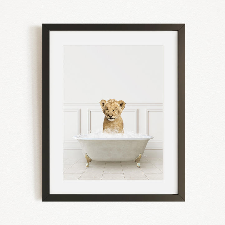 A young lion cub sitting in a white bathtub filled with water, looking directly at the camera.