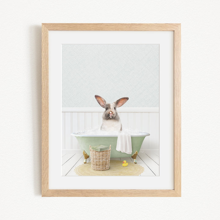 A white rabbit sitting in a green bathtub filled with bubbles, surrounded by a basket of bath toys and a yellow rubber duck.