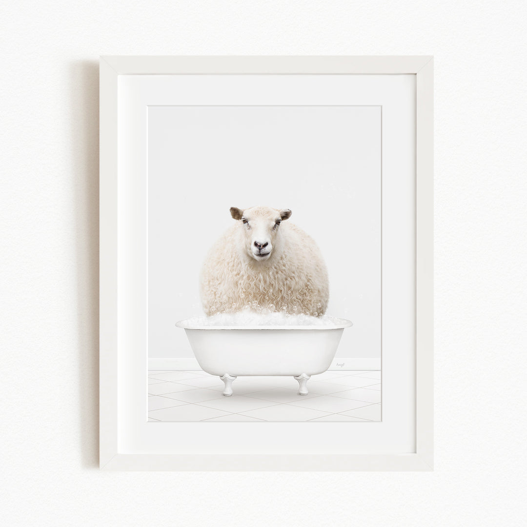 A fluffy white sheep sits in a white bathtub filled with bubbles, looking directly at the camera.