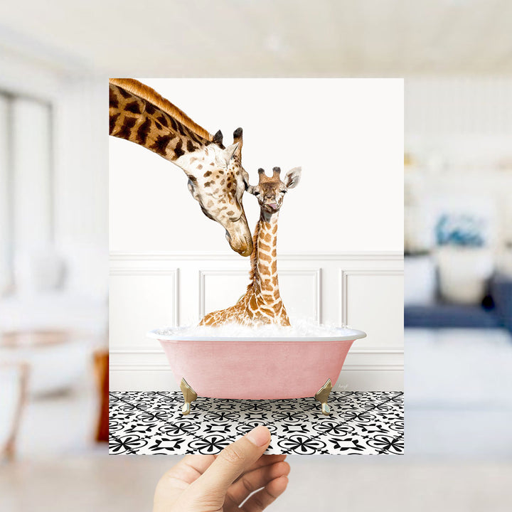 A mother giraffe and her baby giraffe are sitting together in a pink bathtub, with the mother gently licking her baby.