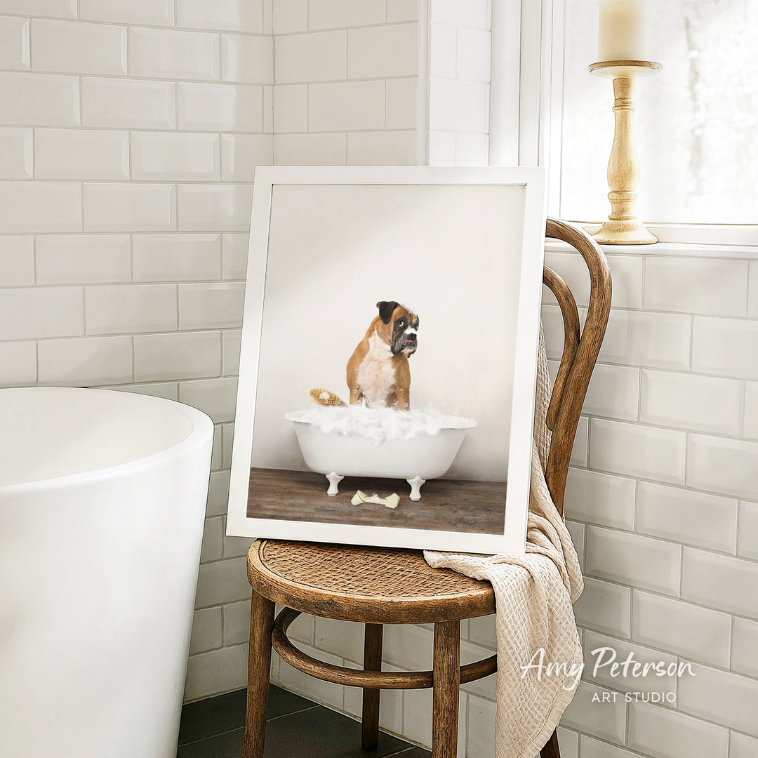 A framed photograph of a dog sitting in a bathtub filled with water, with a towel draped over the back of a wooden chair in the background.