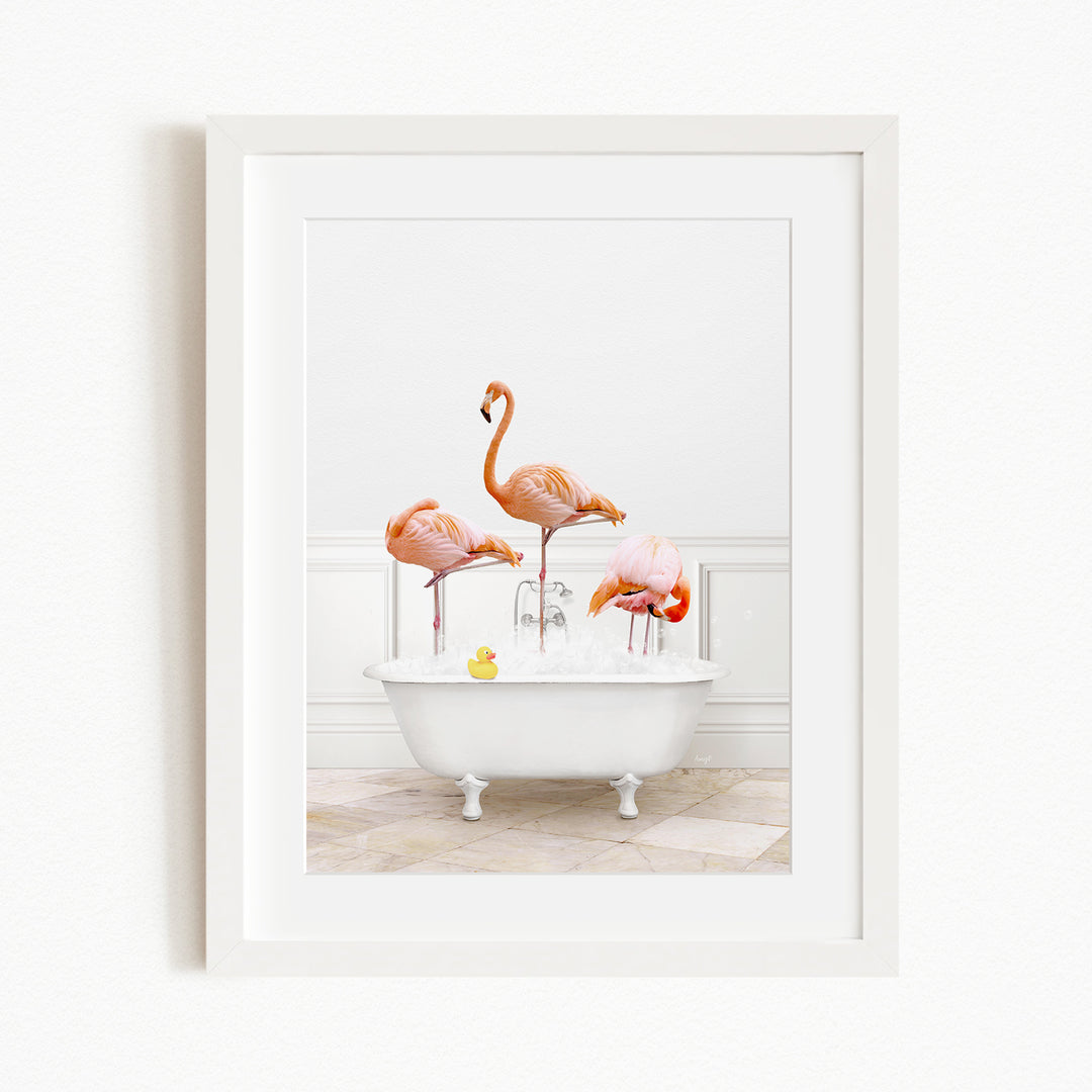 A framed image depicting three flamingos standing in a white bathtub filled with water, with a yellow rubber duck floating in the water.