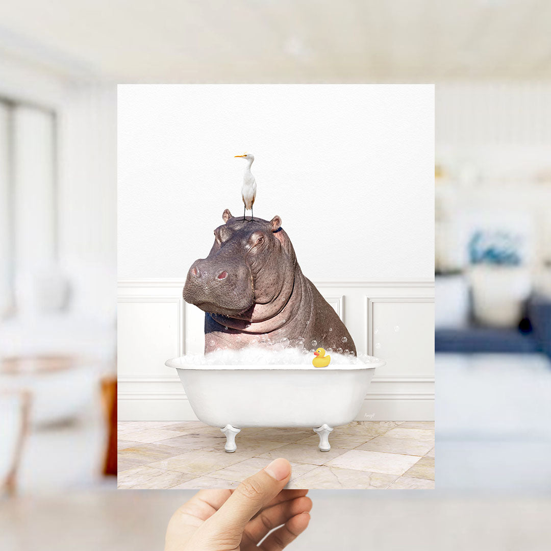 A hand holds up a framed image depicting a hippopotamus sitting in a bathtub, with a seagull perched on its head.