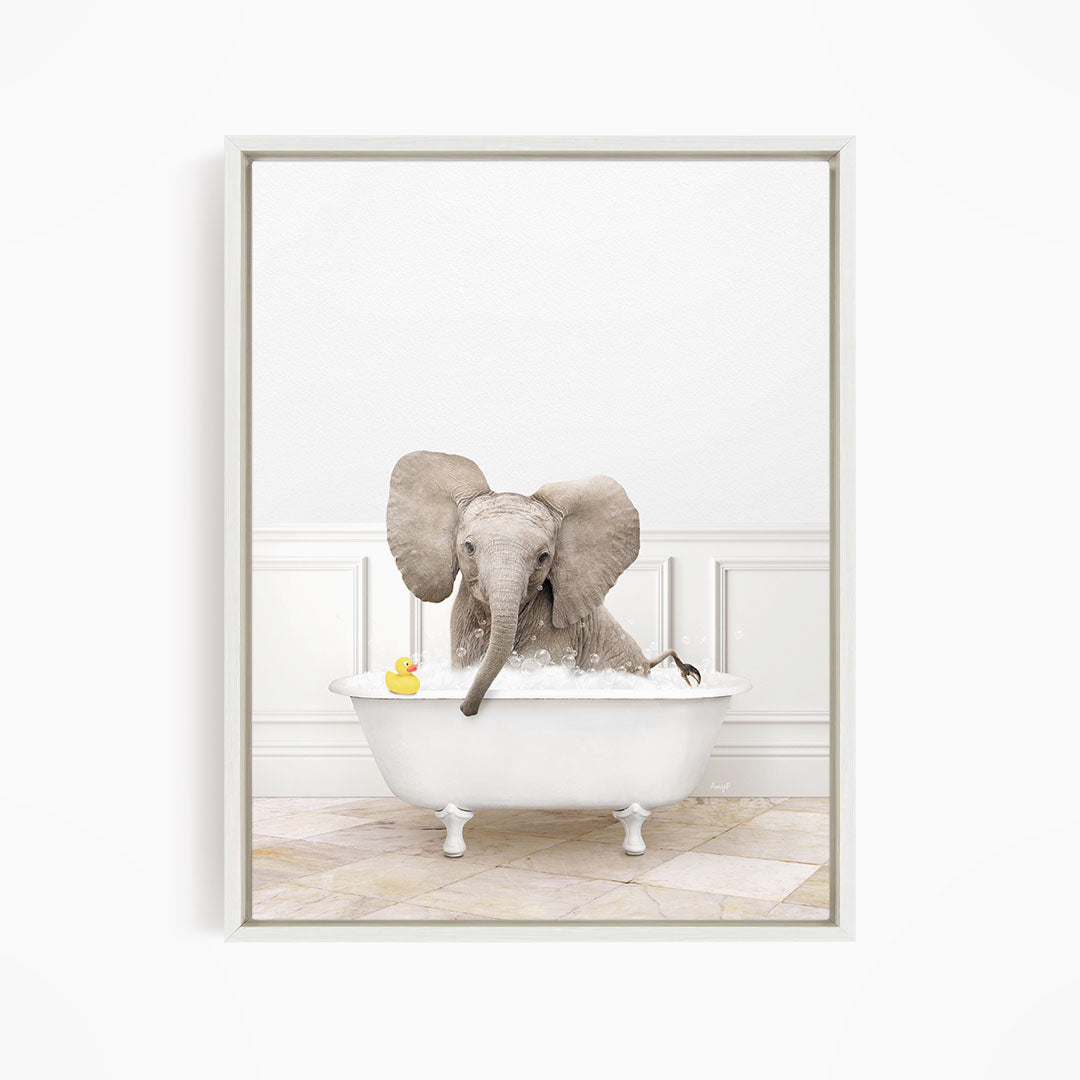 A baby elephant sitting in a white bathtub, with a yellow rubber duck floating nearby.