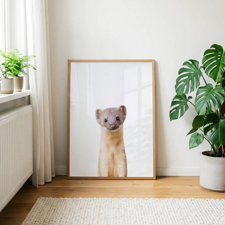 a large framed picture of a cat with a curious expression, placed on a wooden floor in a room with a window and potted plants.