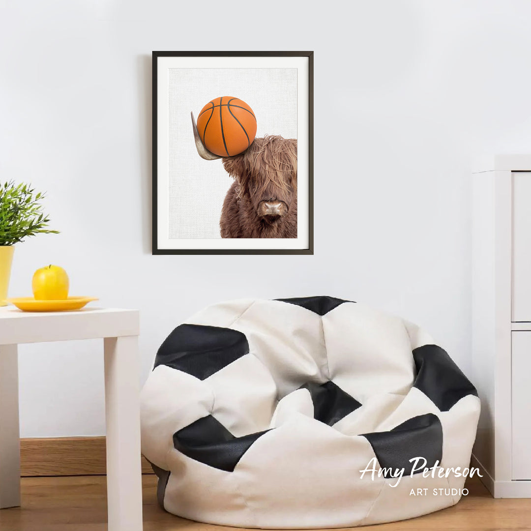a framed picture of a brown cow with a basketball on its head, hanging on a white wall above a black and white bean bag chair.
