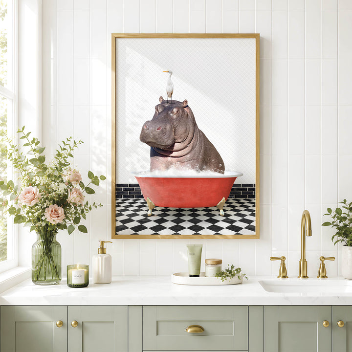 A framed image of a hippopotamus sitting in a red bathtub, surrounded by a black and white checkered floor and a vase of pink flowers, is displayed on a white wall above a bathroom sink.