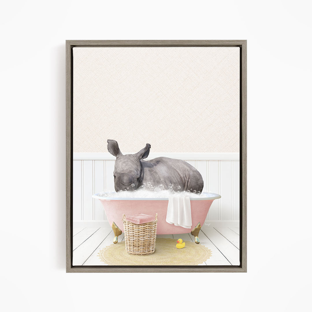 A rhinoceros is sitting in a pink bathtub filled with water, surrounded by a yellow rubber duck and a basket of bath toys.