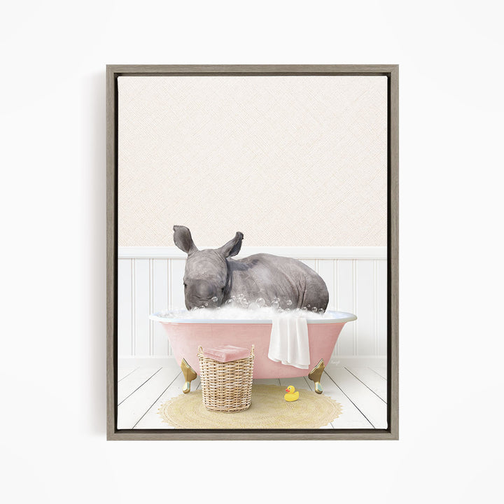 A rhinoceros is sitting in a pink bathtub filled with water, surrounded by a yellow rubber duck and a basket of bath toys.