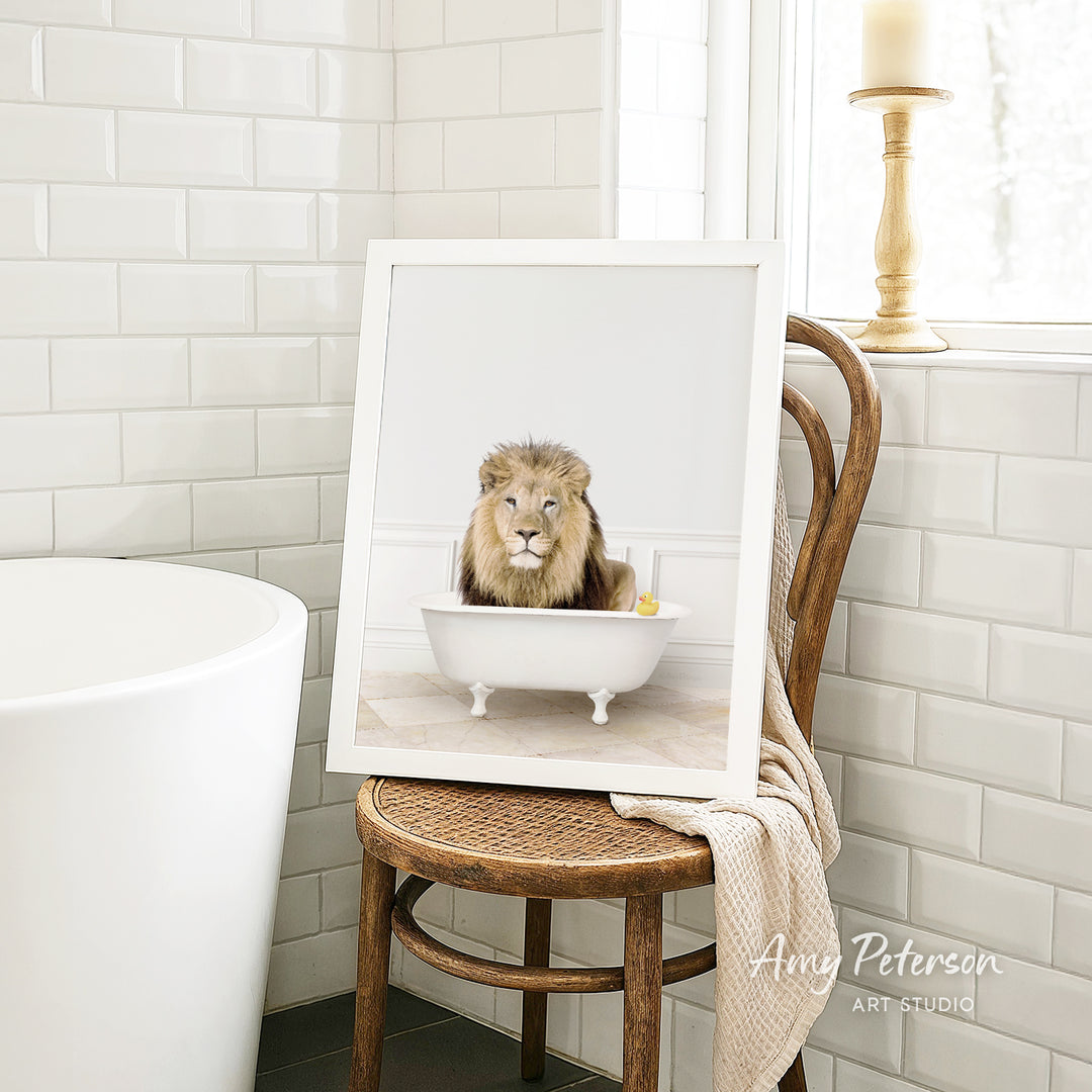 A framed image of a lion sitting in a bathtub, surrounded by a yellow rubber duck, is displayed on a wooden chair in a bathroom setting.