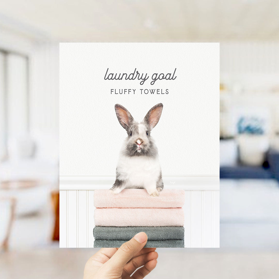 A hand holding a stack of fluffy towels with a cute rabbit sitting on top.