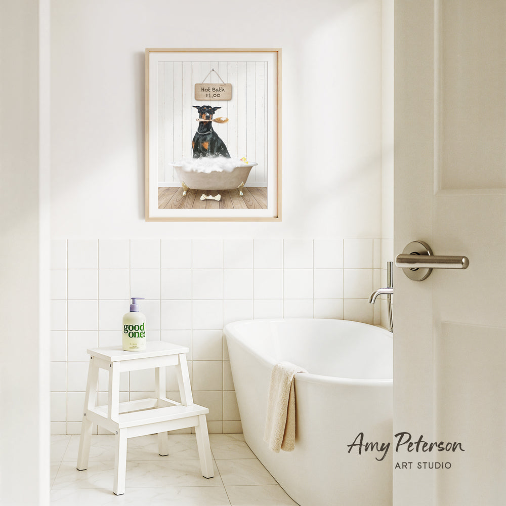 A framed picture of a dog sitting in a bathtub, with a sign above it that says "Hot bath $1.00". The bathroom has a white bathtub, a stool, and a towel hanging on the side of the tub.