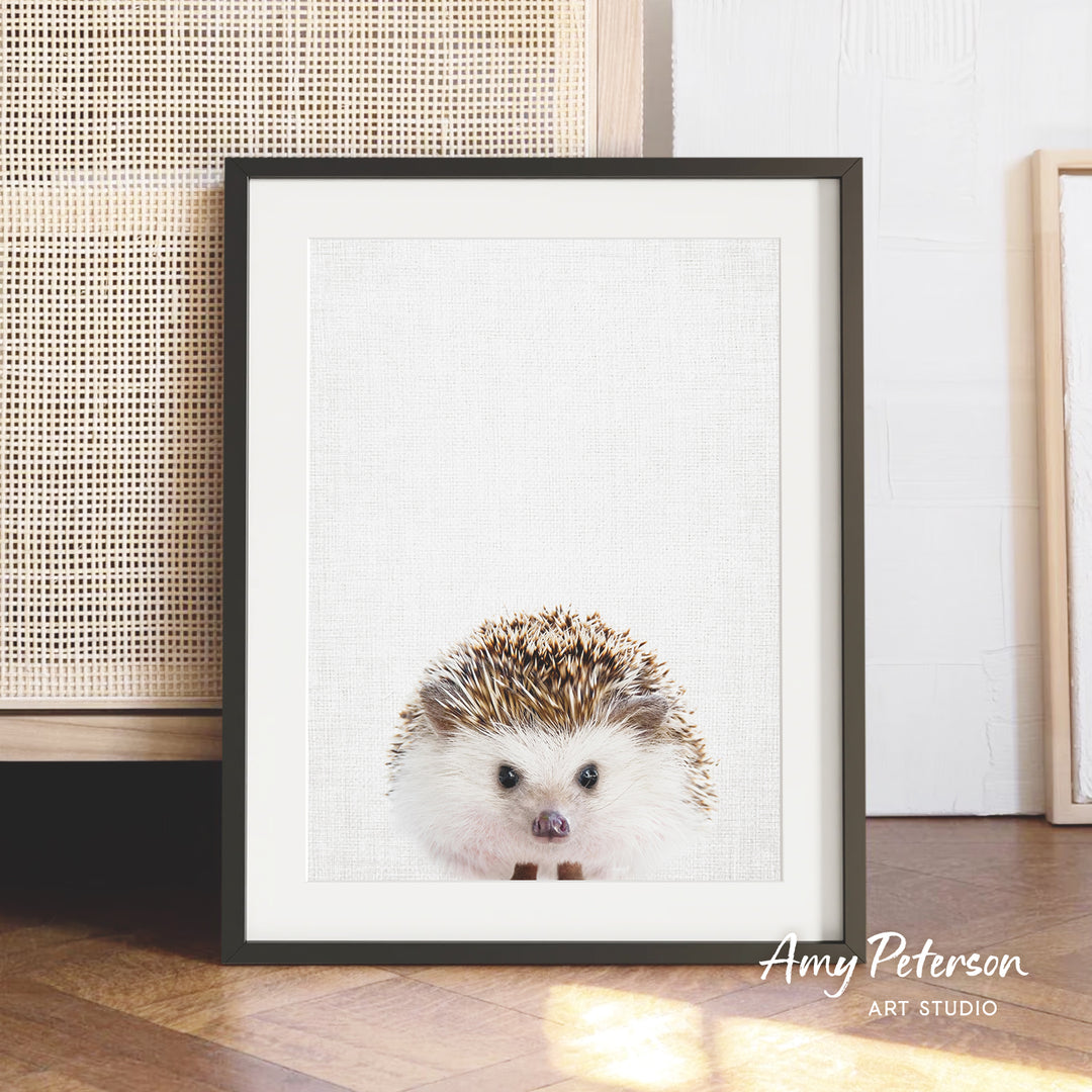 A framed print of a hedgehog is displayed on a wooden floor, with a woven basket visible in the background.