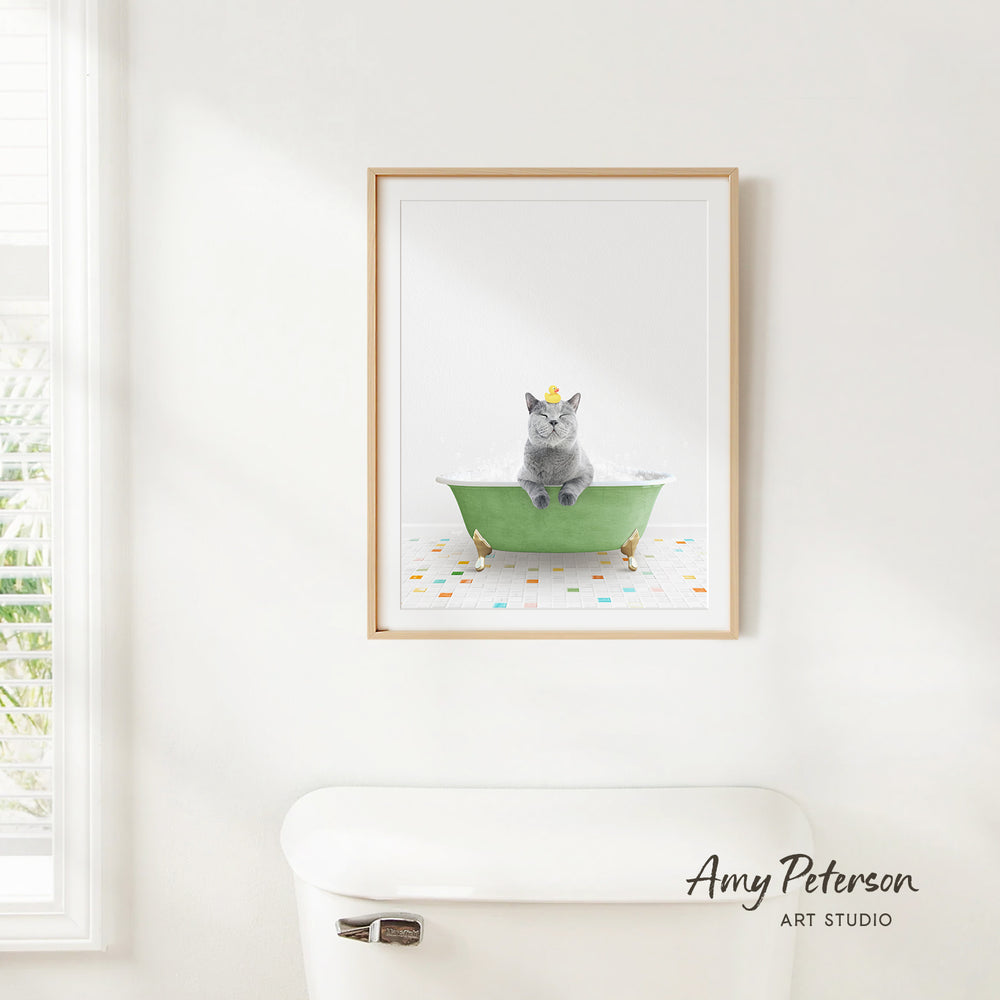 A framed image of a gray cat sitting in a green bathtub, with colorful tiles on the floor.