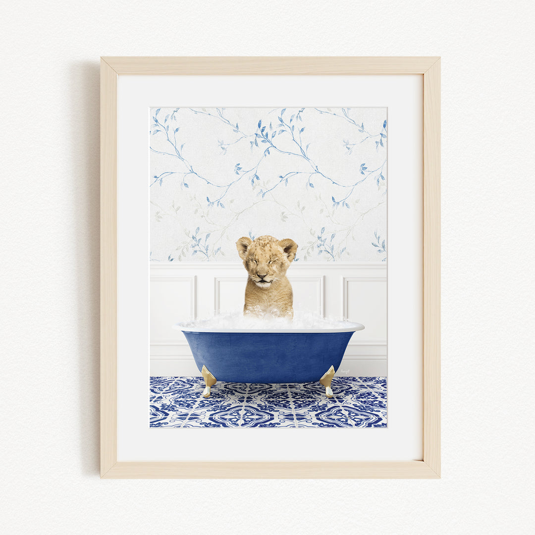 A young lion cub sitting in a blue bathtub filled with water, surrounded by a blue and white patterned rug.