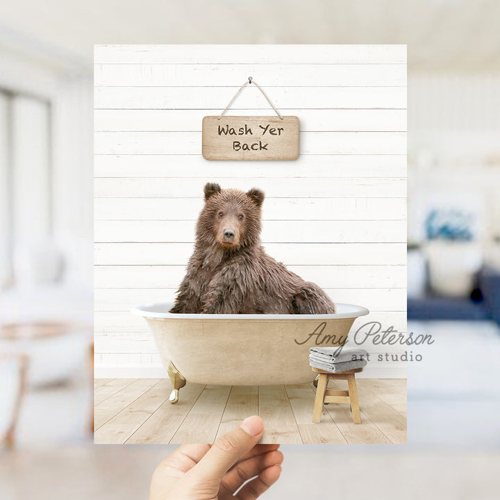 a hand holding a photo of a bear in a bathtub