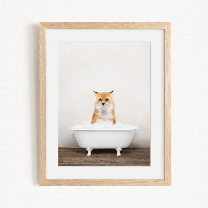 A red fox sitting in a white bathtub filled with bubbles, looking directly at the camera.