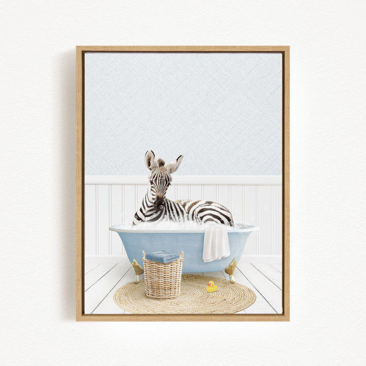 A zebra is sitting in a blue bathtub, surrounded by a basket, a yellow rubber duck, and a white towel.