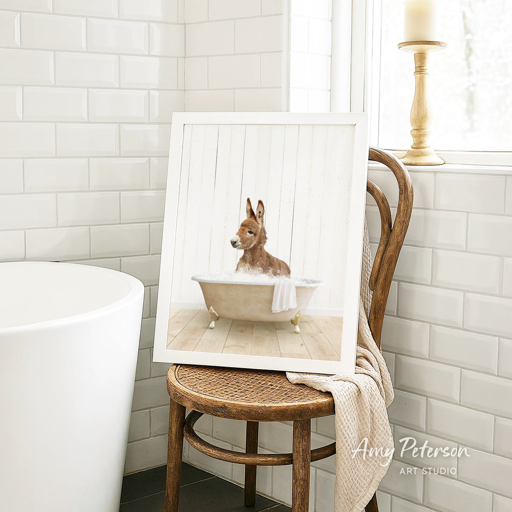 A framed image of a donkey sitting in a bathtub, with a towel draped over the side of the tub.