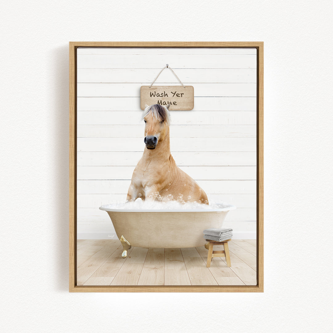 A light brown horse is sitting in a white bathtub filled with bubbles, with a wooden sign above it that says "Wash Your Mane".