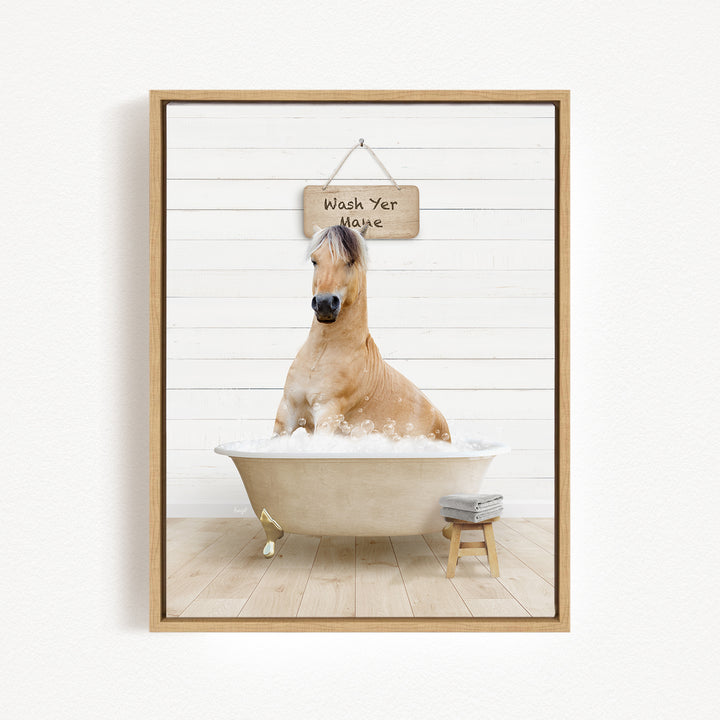 A light brown horse is sitting in a white bathtub filled with bubbles, with a wooden sign above it that says "Wash Your Mane".
