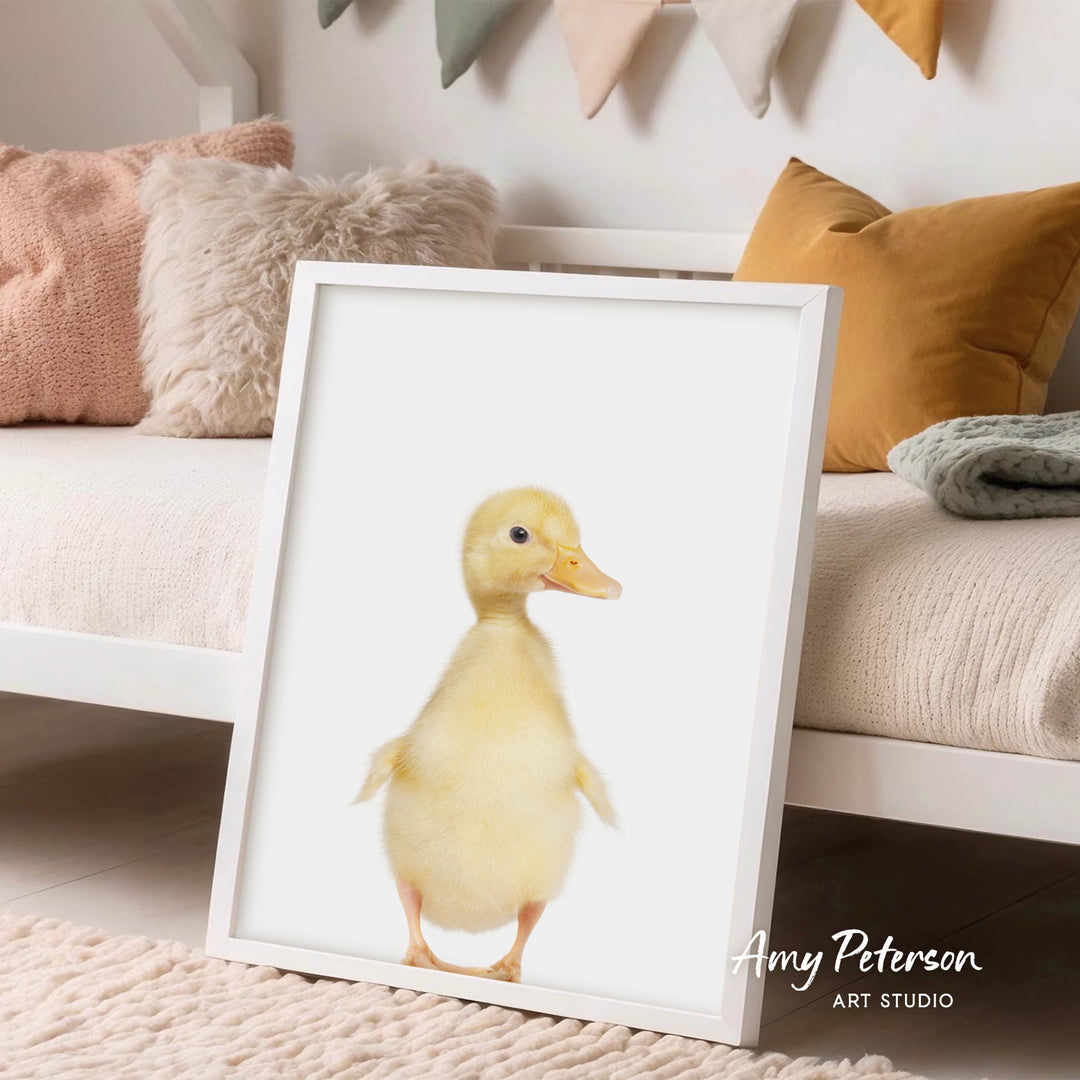 A framed image of a cute yellow duck is displayed on a white wall in a cozy living room setting.