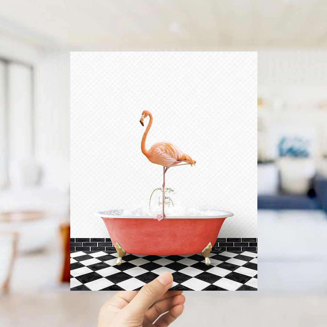 A hand holds up a framed image of a pink flamingo standing on a red bathtub filled with bubbles, set against a black and white checkered floor.