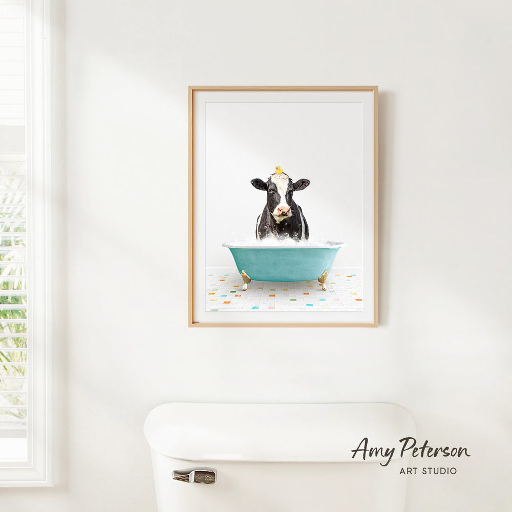 A framed image of a cow sitting in a blue bathtub, with a yellow object on its head, is hanging on a white wall.