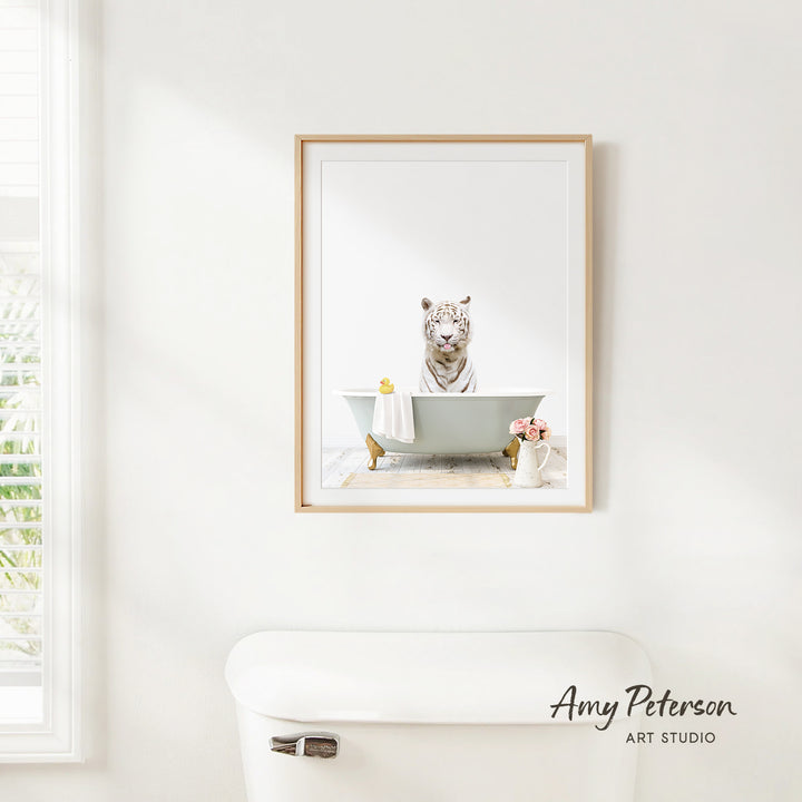 A framed image of a tiger sitting in a bathtub, surrounded by flowers and a vase, is displayed on a white wall in a bathroom.