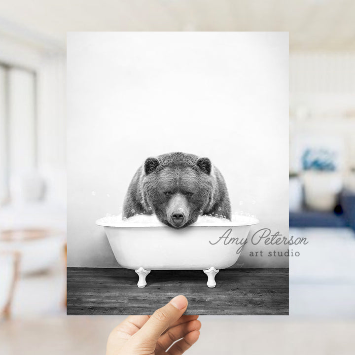 a hand holding up a black and white photo of a bear in a bathtub