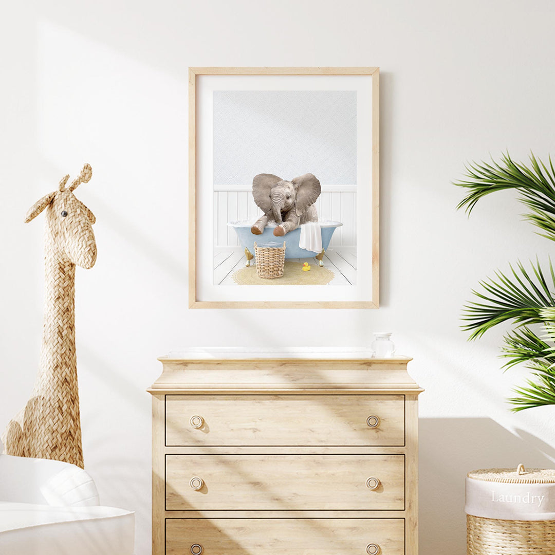 A framed image of an elephant sitting in a bathtub is displayed on a white wall above a wooden dresser.