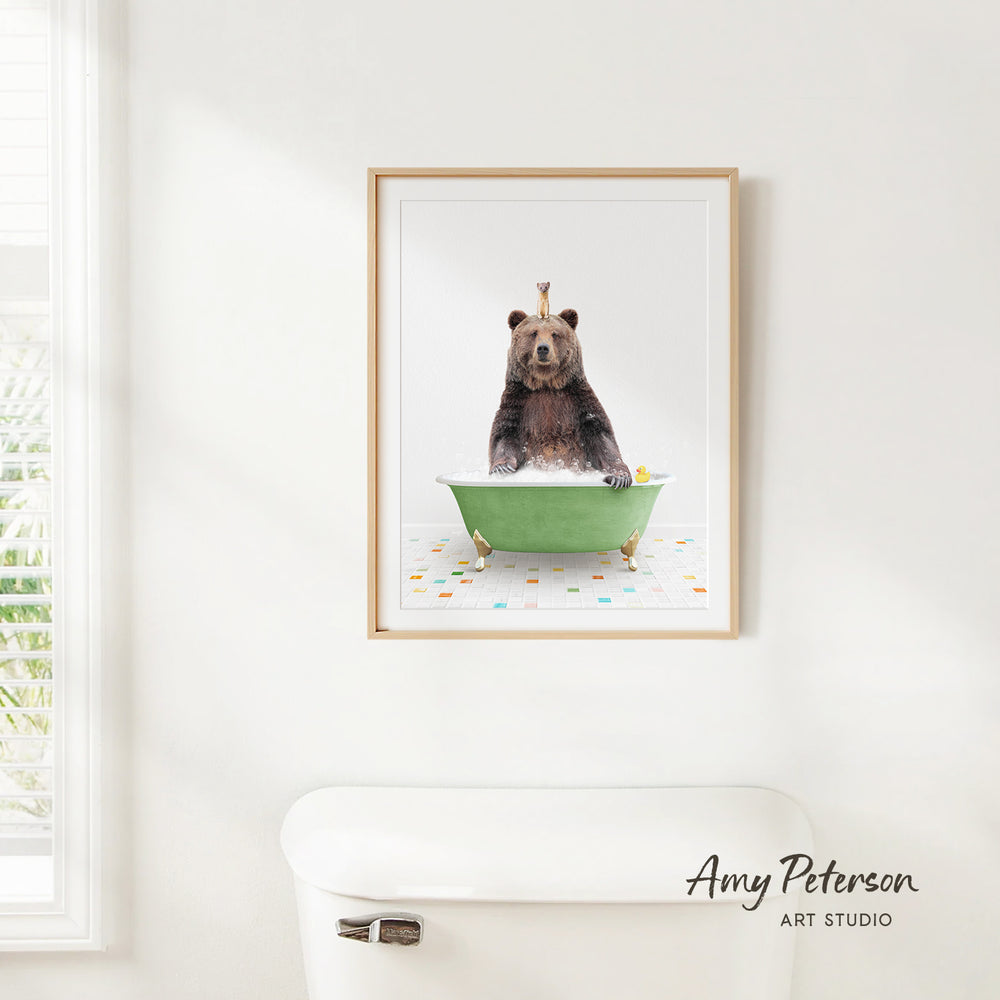 A framed image of a bear sitting in a green bathtub, with a yellow rubber duck floating in the water.