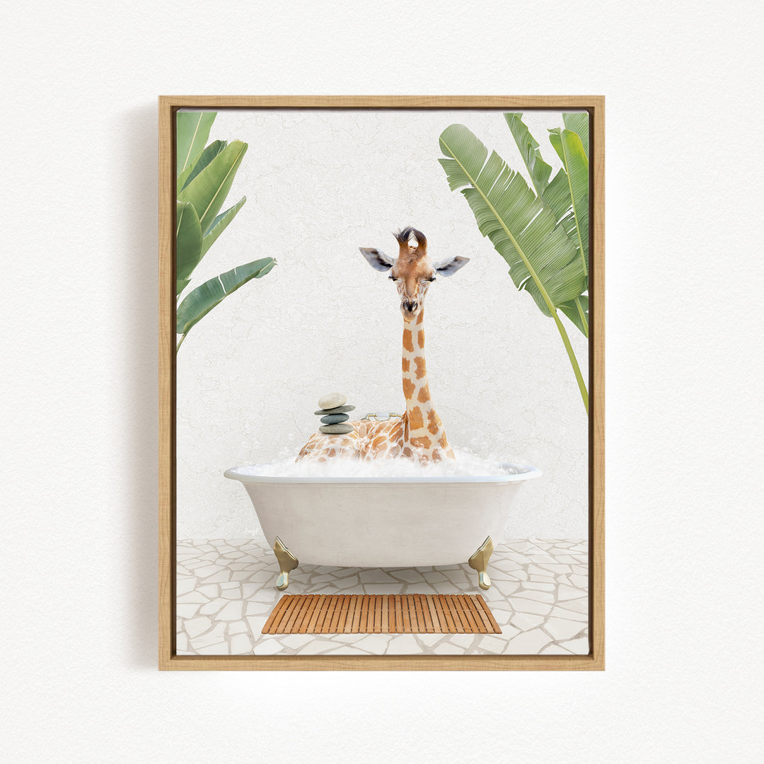 A giraffe is sitting in a white bathtub filled with bubbles, surrounded by green leaves and a wooden mat on the floor.