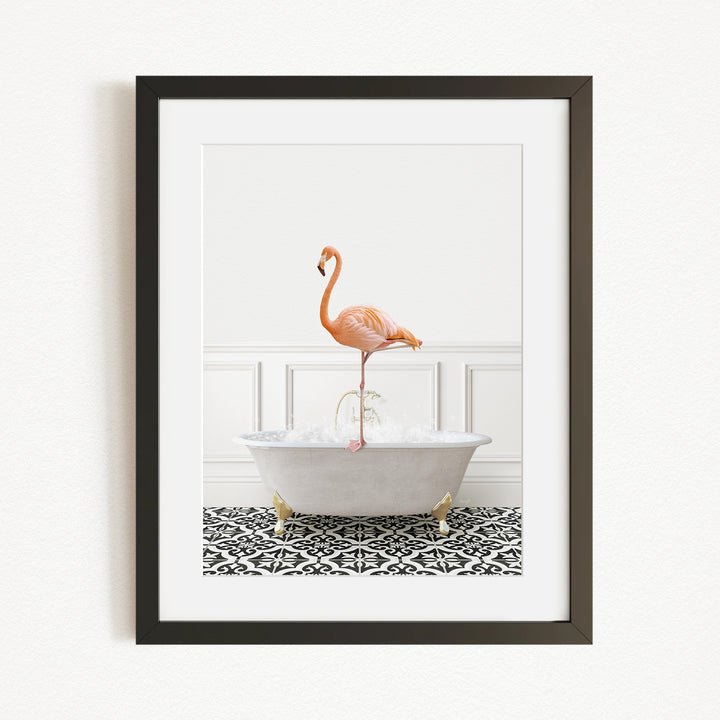 A framed image of a flamingo standing on the edge of a white bathtub filled with water, set against a white wall with a black and white patterned floor.