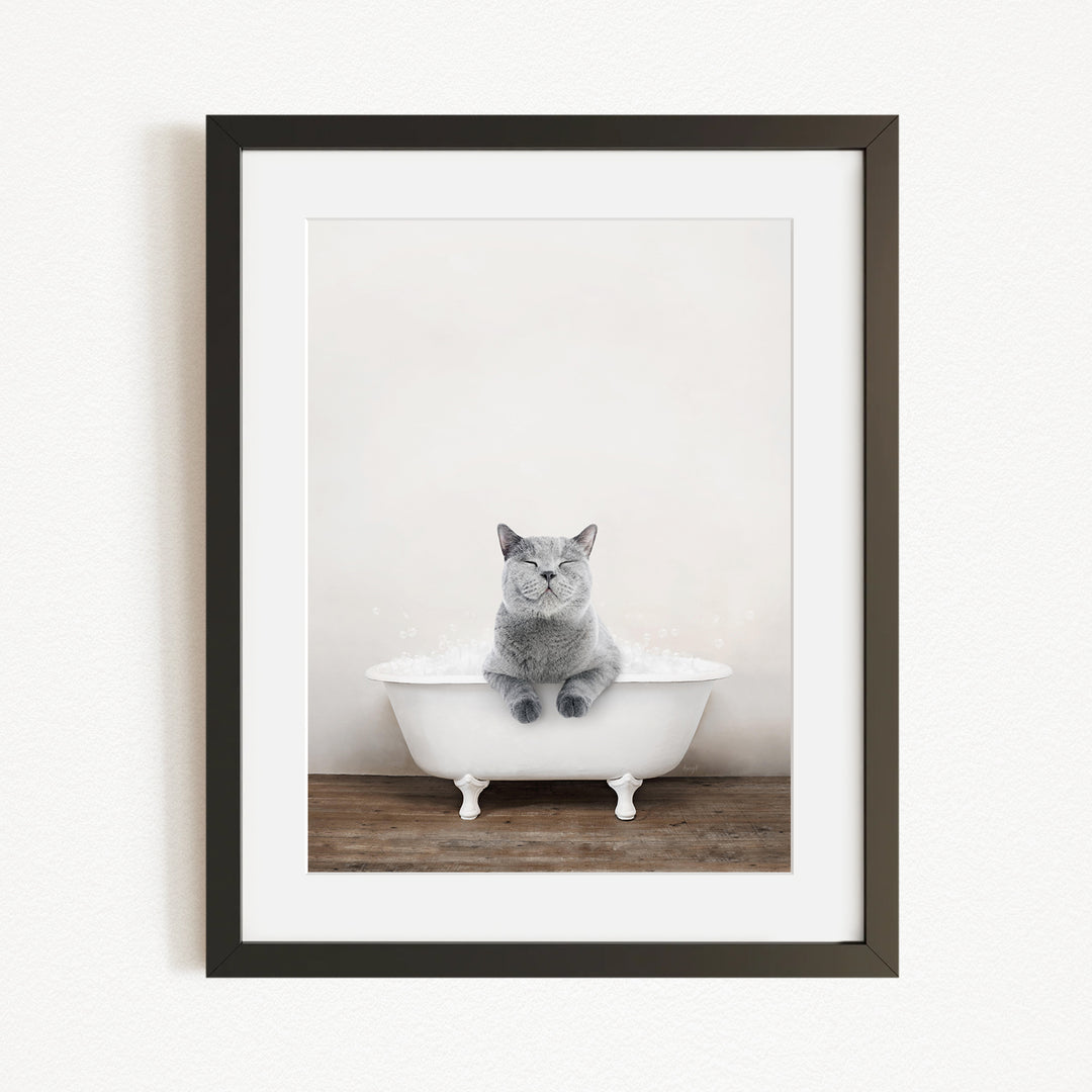 A gray cat sitting in a white bathtub, with a wooden floor beneath it.