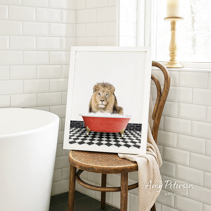 A framed image of a lion sitting in a red bathtub, surrounded by a black and white checkered floor, is displayed on a wooden chair in a bathroom setting.