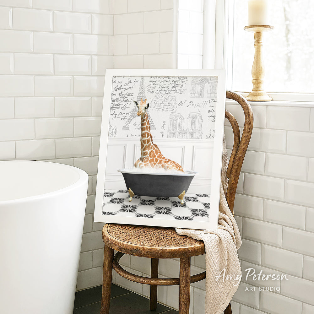 A framed image of a giraffe sitting in a bathtub is displayed on a wooden chair in a bathroom setting.