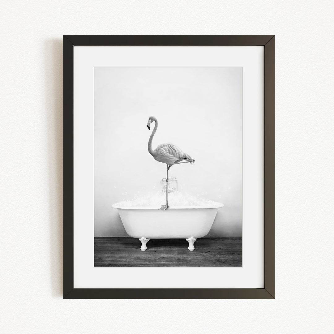 A black and white photograph of a flamingo standing on the edge of a bathtub filled with water.