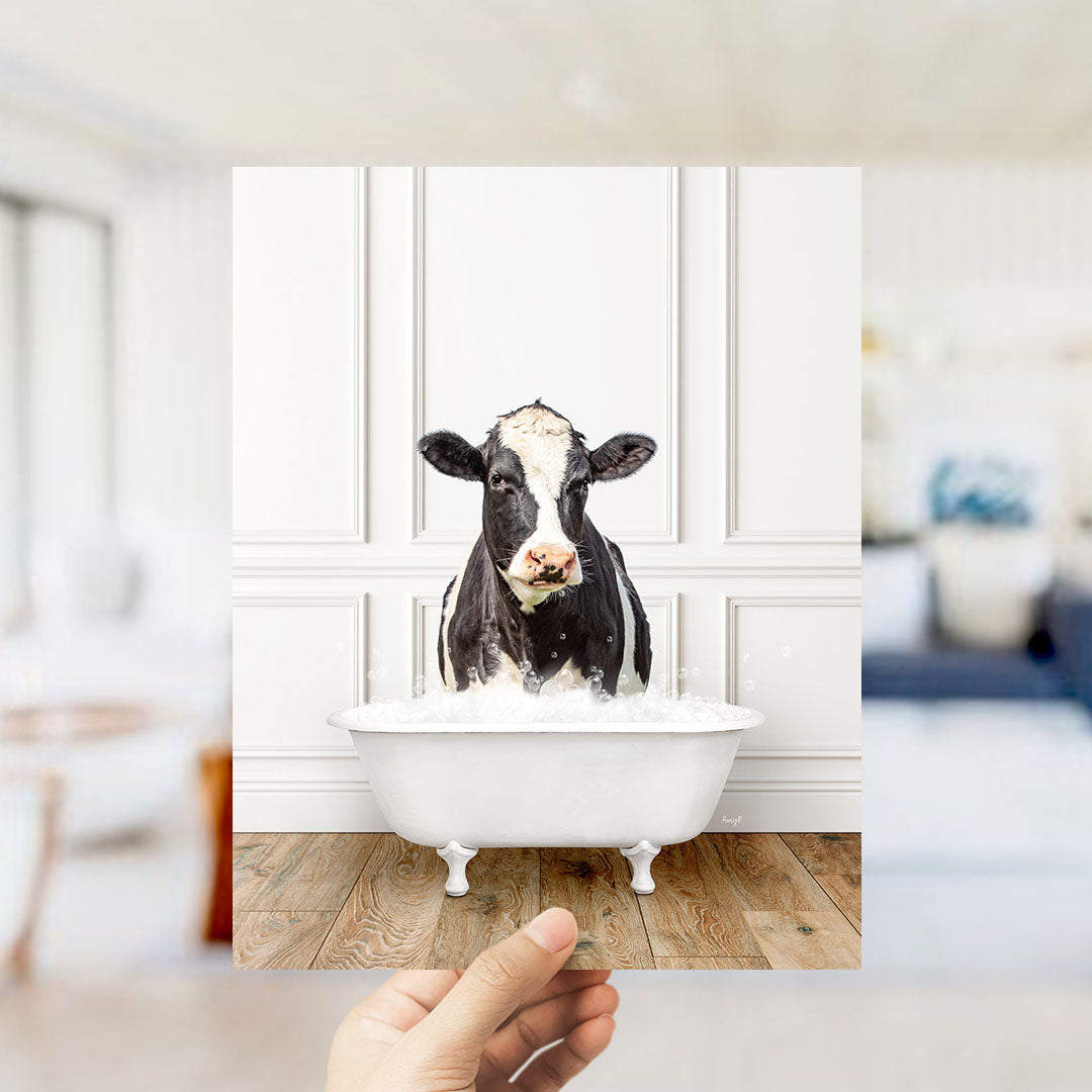 A black and white cow is sitting in a white bathtub filled with water, creating a humorous and unexpected scene.
