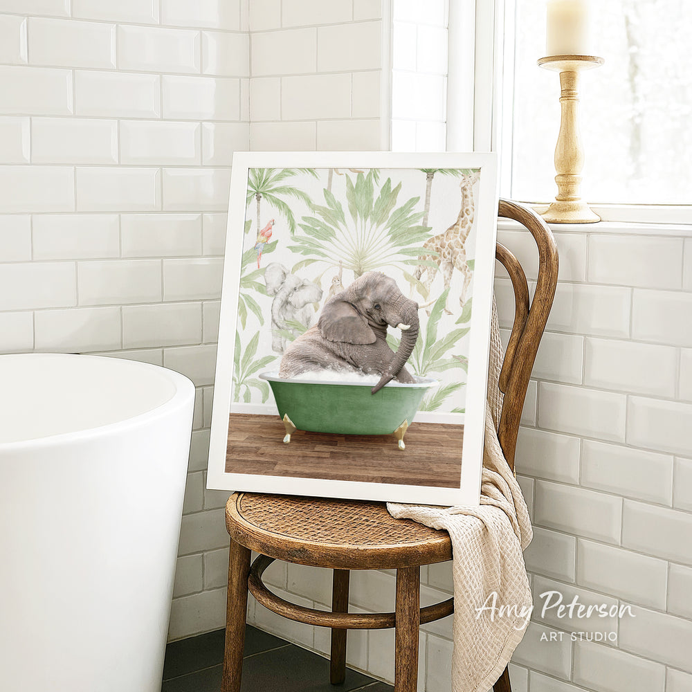 A framed image of a gray elephant sitting in a green bathtub, surrounded by tropical foliage, is displayed on a wooden chair in a bathroom setting.