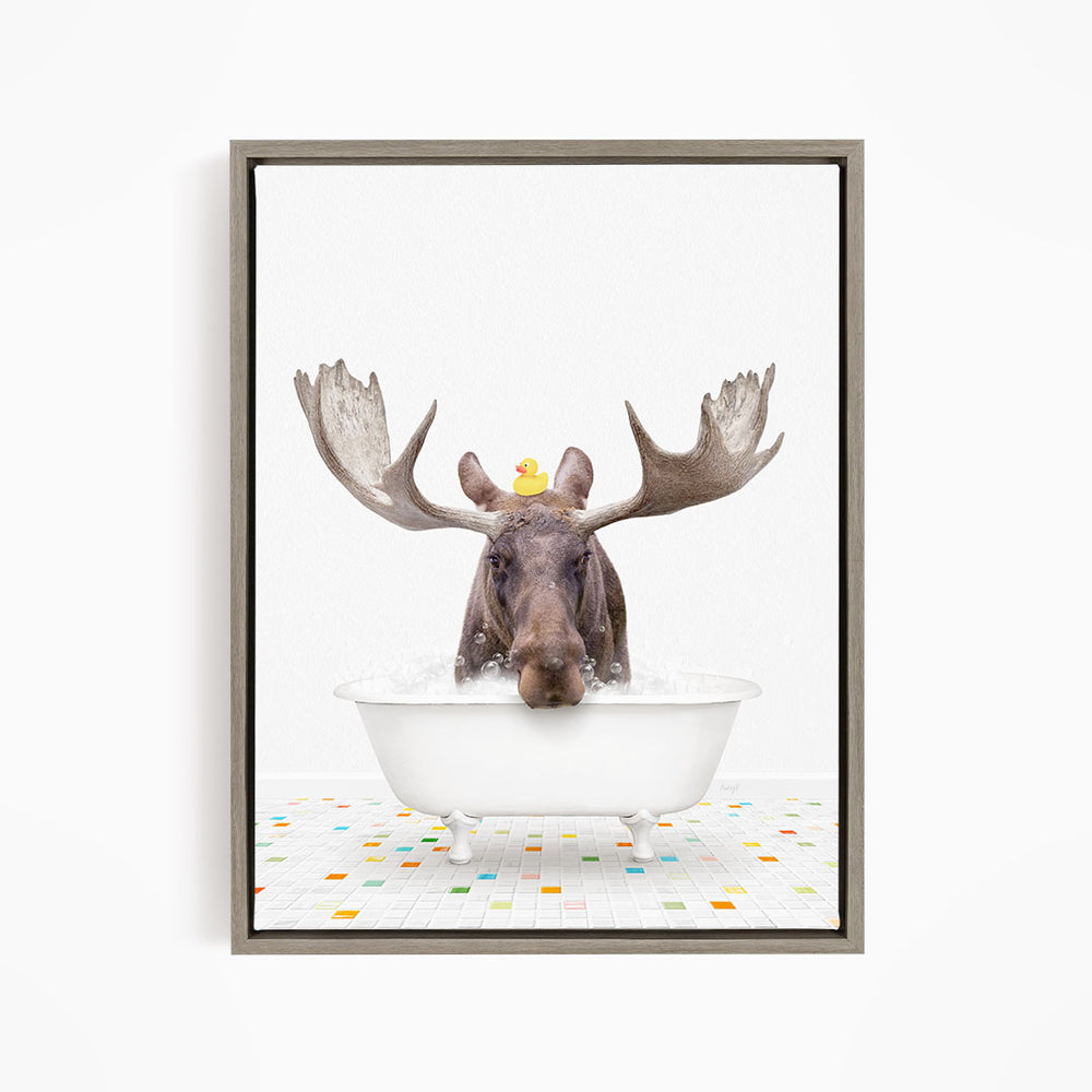 A moose with large antlers is sitting in a white bathtub, with a rubber duck perched on its head.