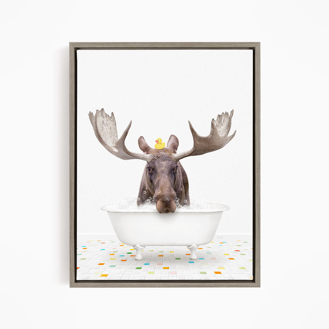 A moose with large antlers is sitting in a white bathtub, with a rubber duck perched on its head.