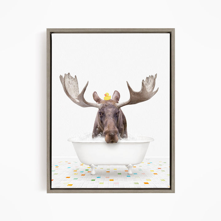 A moose with large antlers is sitting in a white bathtub, with a rubber duck perched on its head.