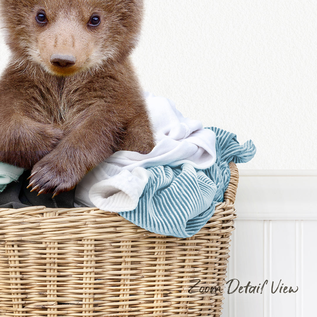 A brown bear sitting in a wicker basket filled with clothes.